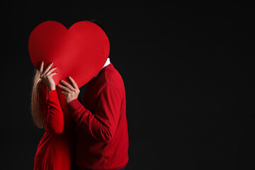 Young couple in love with paper heart on black background. Valentine's Day celebration