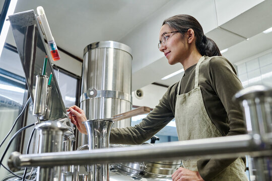 Female worker controlling the working process of equipment during her work in workshop of brewery