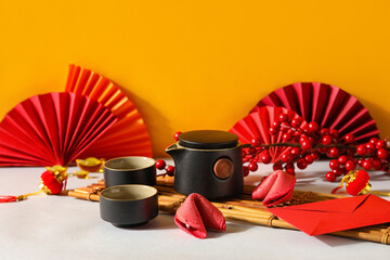 Fortune cookies with teapot, cups and Chinese symbols on table near orange wall. New Year celebration