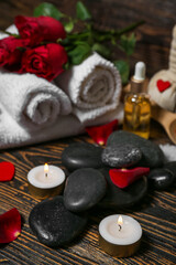 Fototapeta na wymiar Spa stones with candles and rose petals on dark wooden table, closeup. Valentine's Day celebration