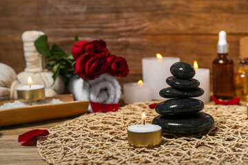 Obraz na płótnie Canvas Spa stones with burning candle on wooden table, closeup. Valentine's Day celebration