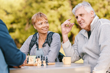 Senior couple playing chess in nature after a wellness, fresh air and health walk in a garden....