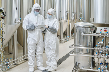 Chemists in protective workwear using tablet pc during their teamwork at chemical factory