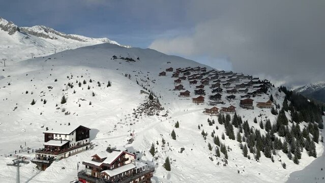 A gondola lift goes up to the Belalp ski resort in Switzerland. In the background are chalets and huts