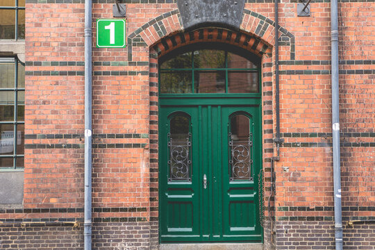 classic green wooden double door in historic red brick building with arched entrance and number one sign above, vintage architecture exterior in old european city street scene