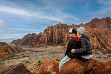 Woman and her son sitting on a rock ledge overlooking beautiful Snow Canyon State park in the deserts of Utah enjoying the view. Family time enjoying nature and being active year round.