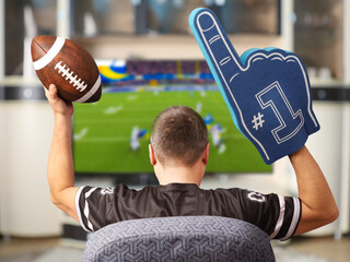 Fan of american football. Man with a ball watching TV.