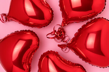 Red inflatable foil balloons in a heart shape on a pink background. Minimal concept.
