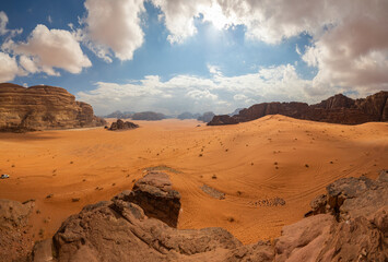 Fototapeta na wymiar Panoramic view of Wadi Rum desert in Jordan with clouds moving over flat sand landscape with mountains in background, 