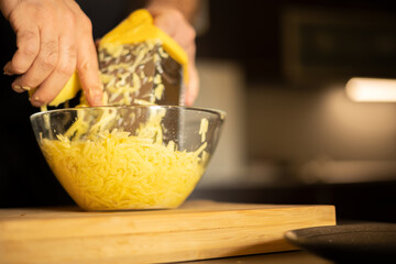 Man's hands with a grater grate the potatoes on the wooden board in glass bowl for potato pancakes in the kitchen. Healthy eating and lifestyle.