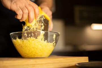 Man's hands with a grater grate the potatoes on the wooden board in glass bowl for potato pancakes in the kitchen. Healthy eating and lifestyle.