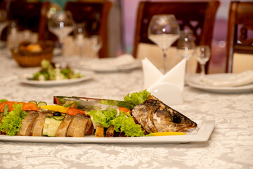 whole fish baked pike perch on a white platter is served in the restaurant.