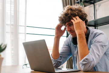 Tired businessman sitting and working with laptop computer, holding head feeling headache