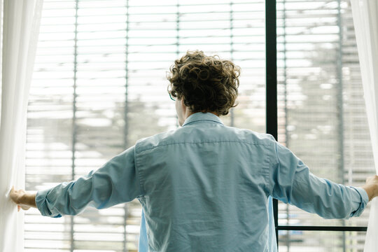 Young Man From Behind Opens The Window Curtains And Looks Out From His Workplace