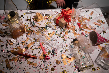 Confetti, empty bottles and party hats on a white table. After party concept