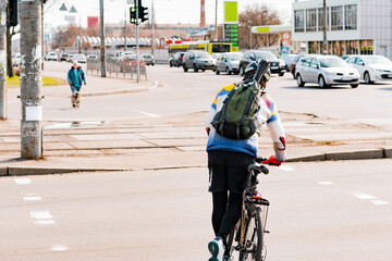 Naklejka premium A man with a backpack and helmet crosses the road with a bike by pushing with one leg. Crosswalk. Pedestrian. Cross. Street. City. Outdoor