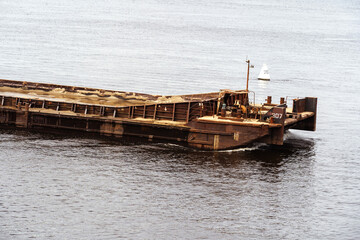A fragment of a rusty barge floating on the river. Cargo ship for transporting sand and other dry...