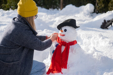 Caucasian woman sculpts a snowman from the snow. The carrot is the place of the nose.