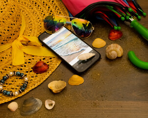 the straw hat lies on the floor in sunlight, next to the phone, shells and glasses. Holiday theme