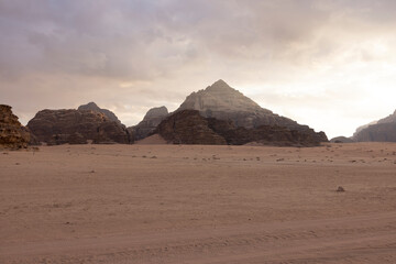 Fototapeta na wymiar Panoramic sunset view of Wadi Rum desert in Jordan with clouds moving over flat sand landscape with mountains in background, 