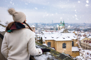 A tourist woman enjoys the panoramic view of the snow covered skyline of Prague, Czech Republic,...