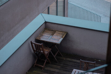 Two empty deck chairs on wooden balcony hiding behind the bushes in winter or rainy time. Solitude and emptiness on the porch. Gray dull setting.