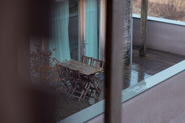 Empty set of deck chairs on wooden balcony hiding behind the bushes in winter or rainy time....
