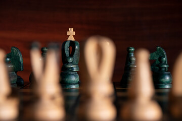 Black king with white cross in background between white chess pieces out of focus with brown wooden background. Concept: chess