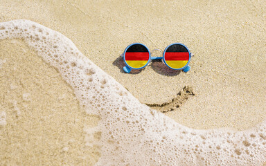 Sunglasses with flag of Germany on a sandy beach. Nearby is a sea lightning and a painted smile. Travel and vacation concept for Germans
