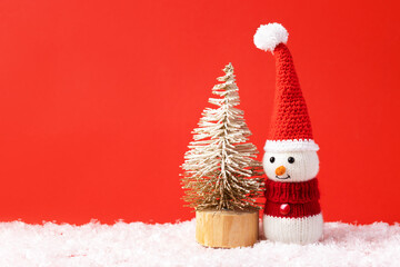 Christmas fairy tale composition of a knitted snowman in a Santa Claus hat and sweater. Small Christmas tree.