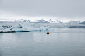 A boat sails through the Jökulsárlón glacier lagoon in Iceland past icebergs that have broken away from the glacier tongue Breiðamerkurjökull. With a view of Hvannadalshnúkur.