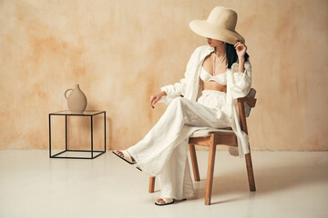 Unrecognizable luxurious lady on chair in hat sitting on background with textured copy space wall