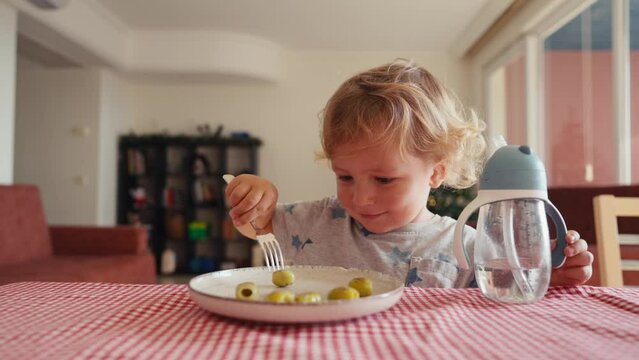 Little cute kid with appetite eats olives itself with fork.