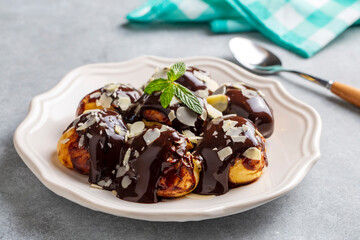 Delicious profiteroles with chocolate and white plate. Selective focus image on light background.