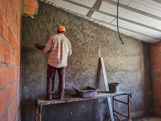 Trabalhador pedreiro a colocar cimento no muro para finalizar a parede com o reboco