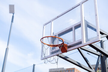 outdoor basketball in front of a blue sky. The basketball hoop or ring is orange and its pole is...