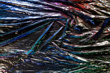 Black color plastic wrap background. Dark crumpled wrinkled plastic cellophane. Reflecting colorful...