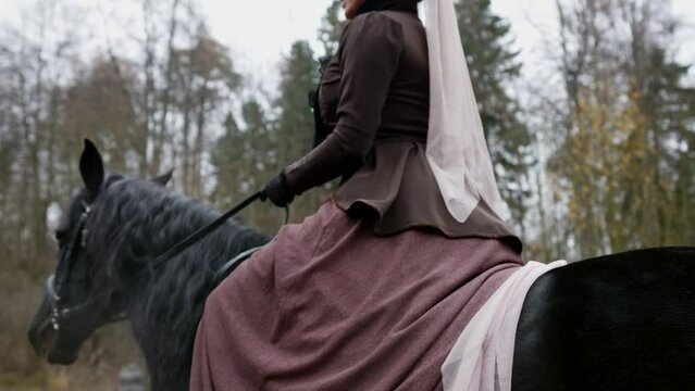 elegant woman in old historical dress of 19 century ride black horse in park, history and vintage
