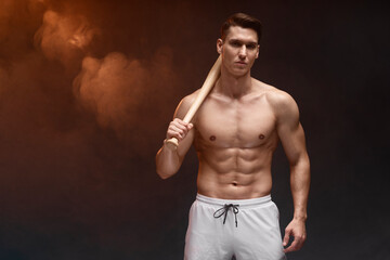 Close-up portrait of muscular man posing with bat at studio alone
