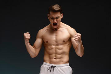 Fototapeta na wymiar Athletic fitness model screaming and demonstrating muscles while posing