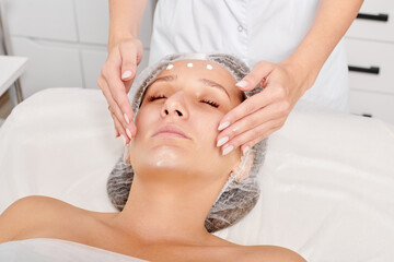 Beautician rubbing moisturizing cream mask into woman face skin for rejuvenation, anti aging...