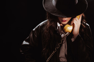 Dark noir portrait of a female detective holding a retro telephone receiver. Private detective, spy, investigation concept. - obrazy, fototapety, plakaty