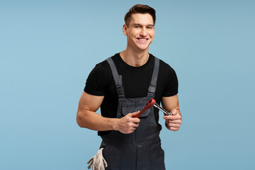Smiling young mechanic holding a wrench isolated on blue background