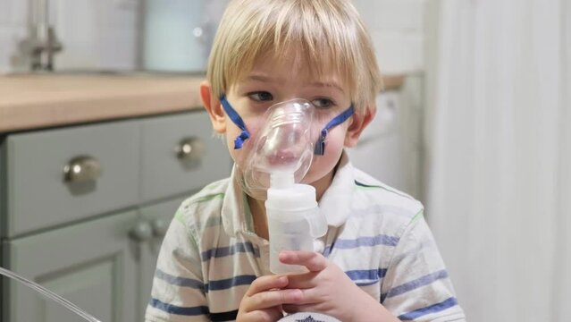 Sick Baby Boy with making Inhalation with a Mask on his Face sitting in Living Room at Home. Children Healing. Child Inhalation therapy with Compressor nebulizer. Inhaling fumes medication into lungs