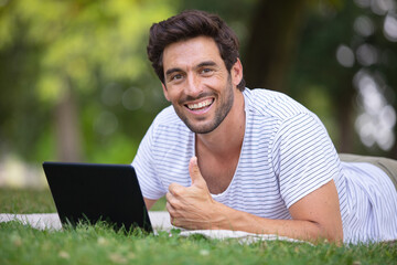 happy man sitting on the grass is working on laptop