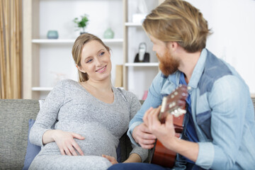 pregnant woman smiling to husband while playing the guitar