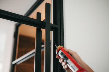 Builder Hands applying black silicone sealant while installing a door assembly