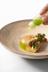 Fine dining dish on marble table in fine dining restaurant with hand adding oil