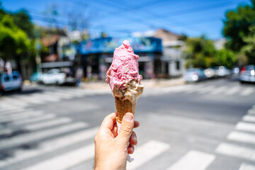 Ice cream in hand. Waffle cone with ice cream on the background of the street in the summer on a hot day. Street food, sweets, desserts concept.