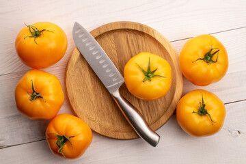 Several natural yellow tomatoes with a knife and a tray, close-up, on a painted wooden table, top view.